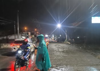 Hujan Mengguyur, Bhabinkamtibmas Desa Lingga Tetap Siaga Atur Lalu Lintas di Jalan Lintas Sumatera